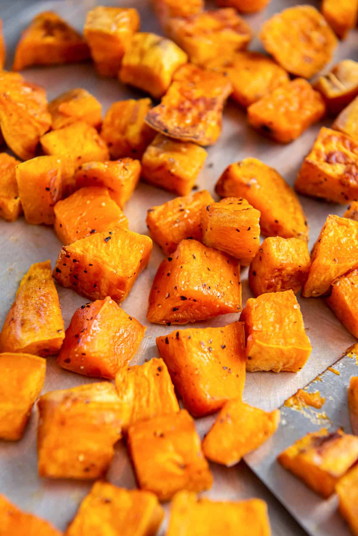 Crispy roasted sweet potatoes cooked on a sheet pan with a spatula for serving.
