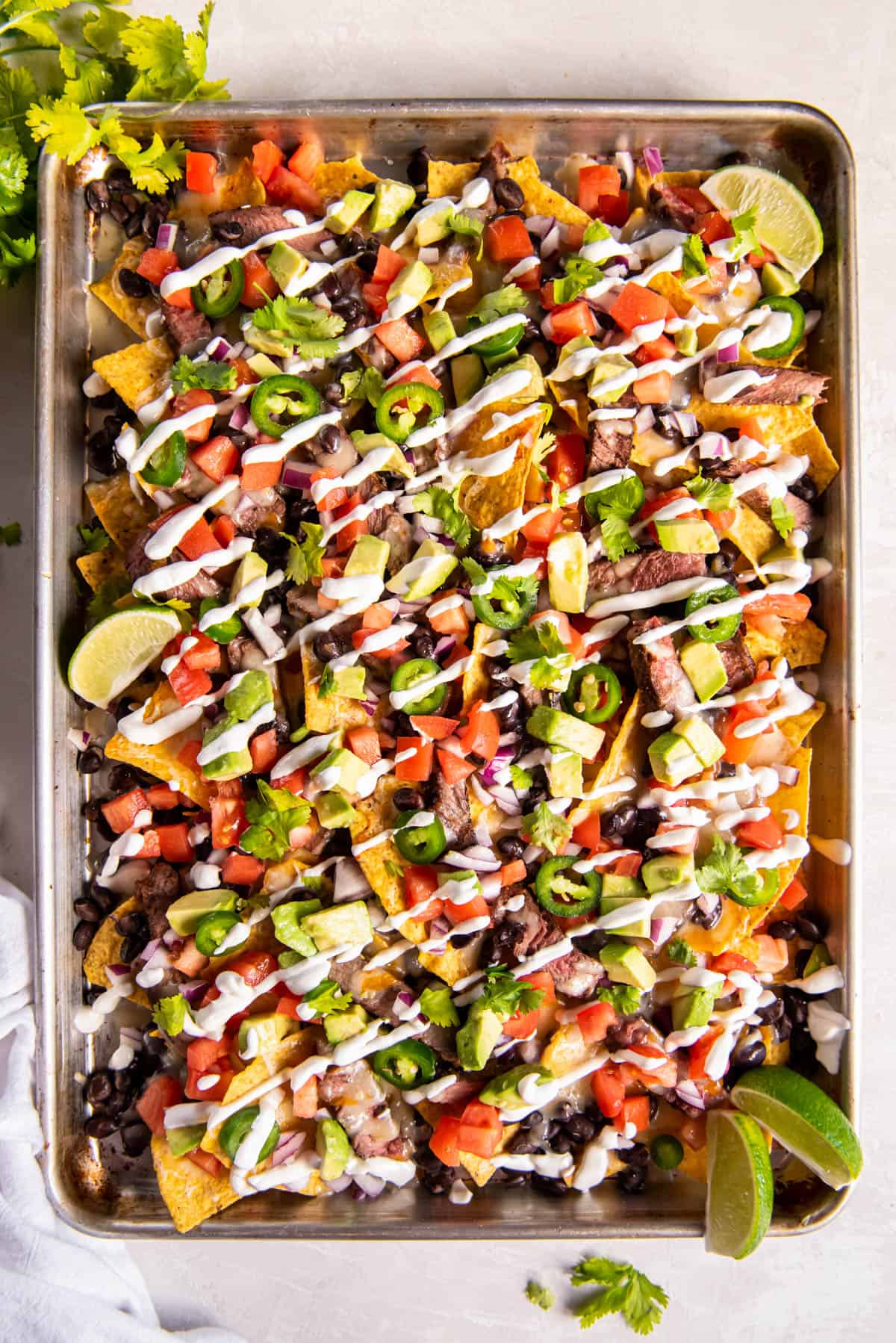 Cooked nachos being served on a sheet pan with nachos toppings like cilantro and sour cream.