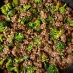 Cooked ground beef and broccoli in a skillet with sesame seeds and sliced green onions garnished on top.