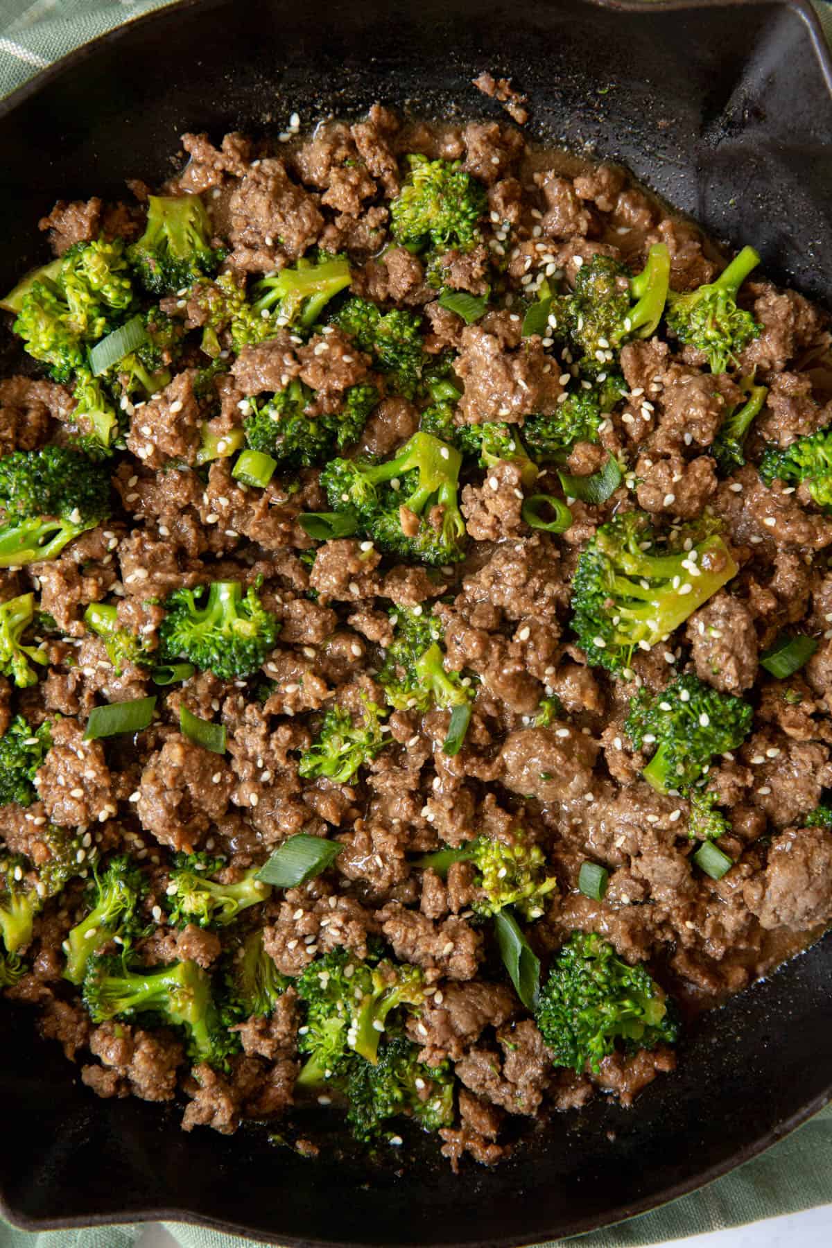 Cooked ground beef and broccoli in a skillet with sesame seeds and sliced green onions garnished on top.