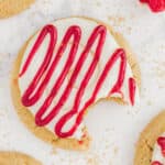 A raspberry cheesecake cookie on a white countertop with a bite taken out of it.