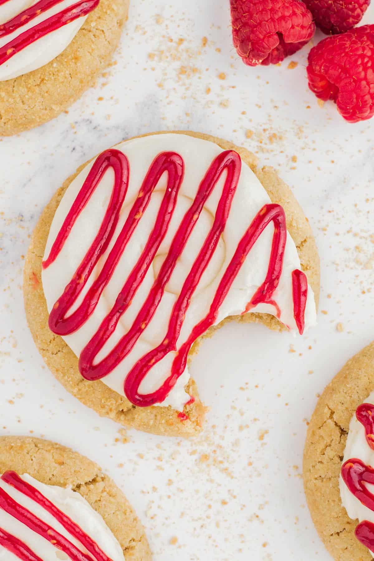 A raspberry cheesecake cookie on a white countertop with a bite taken out of it.