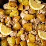 Cooked Italian chicken and potatoes in a skillet ready for serving. Lemon wedges are garnished on top.