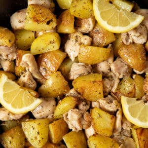 Cooked Italian chicken and potatoes in a skillet ready for serving. Lemon wedges are garnished on top.