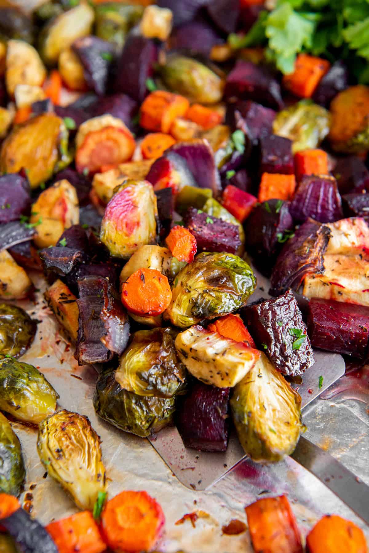 A spatula is scooping honey roasted vegetables off of a sheet pan for serving.