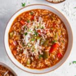 A bowl of instant pot stuffed pepper soup sitting on a white countertop with a bowl of fresh parmesan cheese on the side.
