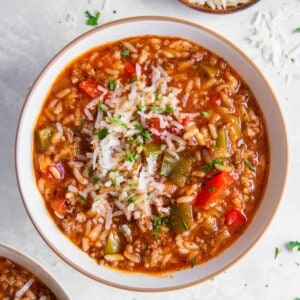A bowl of instant pot stuffed pepper soup sitting on a white countertop with a bowl of fresh parmesan cheese on the side.