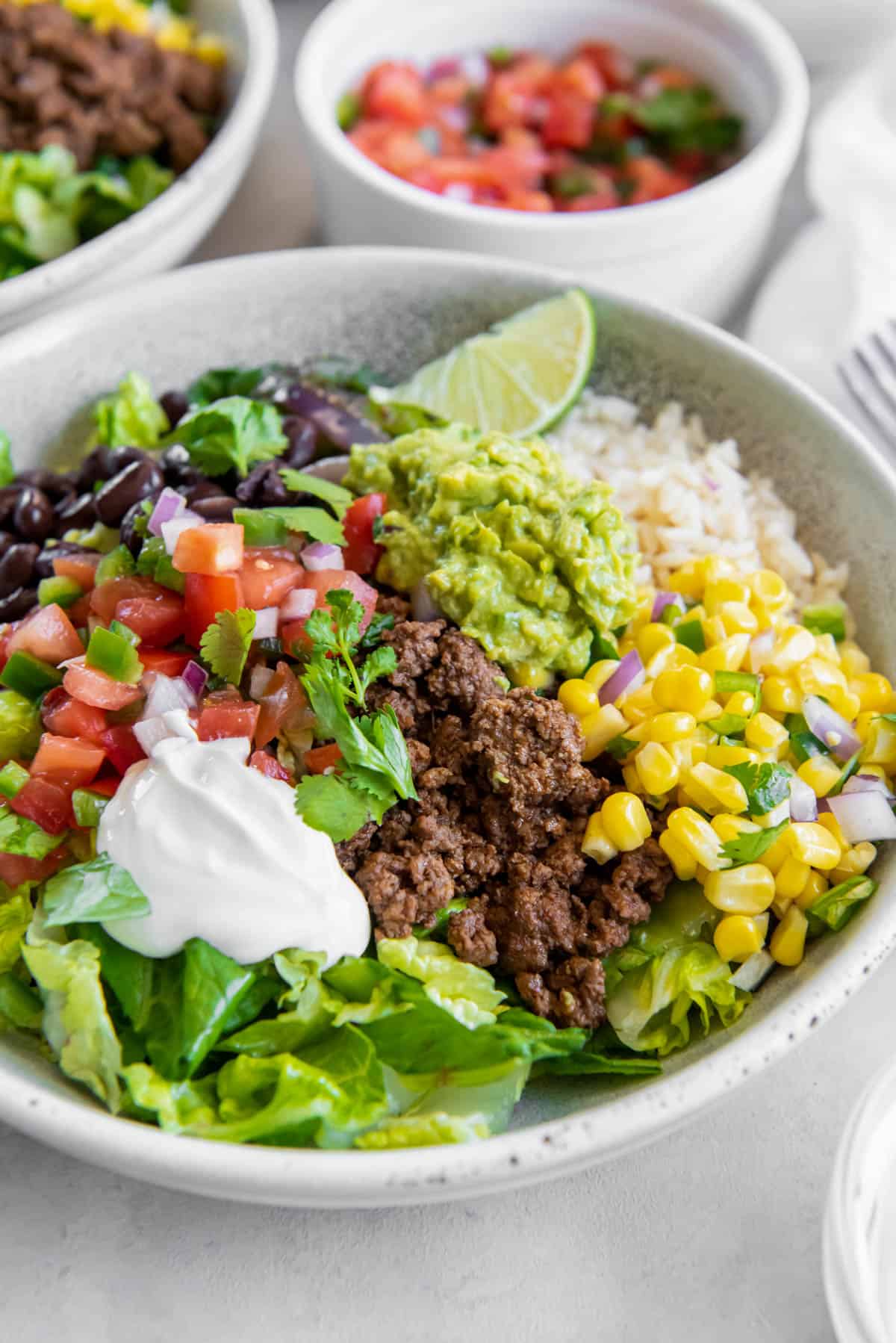 A ground beef burrito bowl with burrito toppings including cilantro, sour cream and guacamole. It's sitting on a table ready to eat.