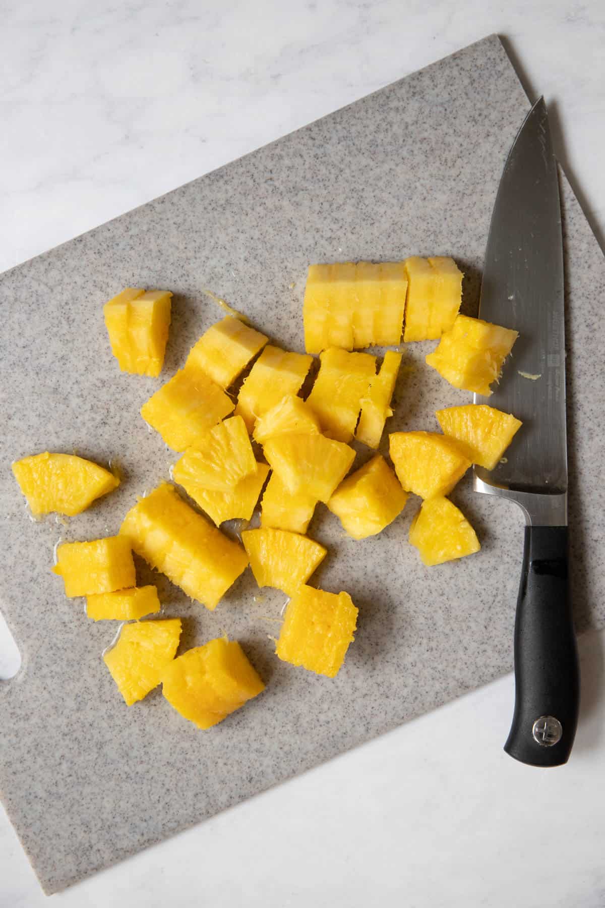 Pieces of cut pineapple on a cutting board with a sharp knife.