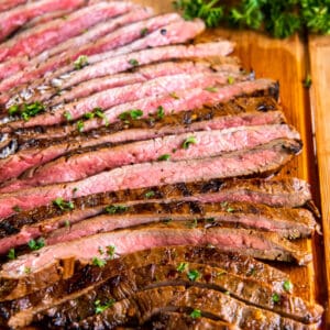 A wooden cutting board with slices of cast iron flank steak ready to be served.