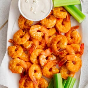 A white plate filled with buffalo shrimp and celery.