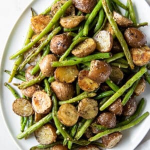 Oven roasted green beans and potatoes on a oval round plate ready for serving.