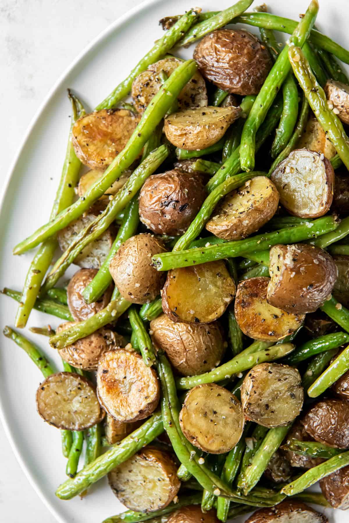 Roasted green beans and potatoes on a white plate ready for serving.