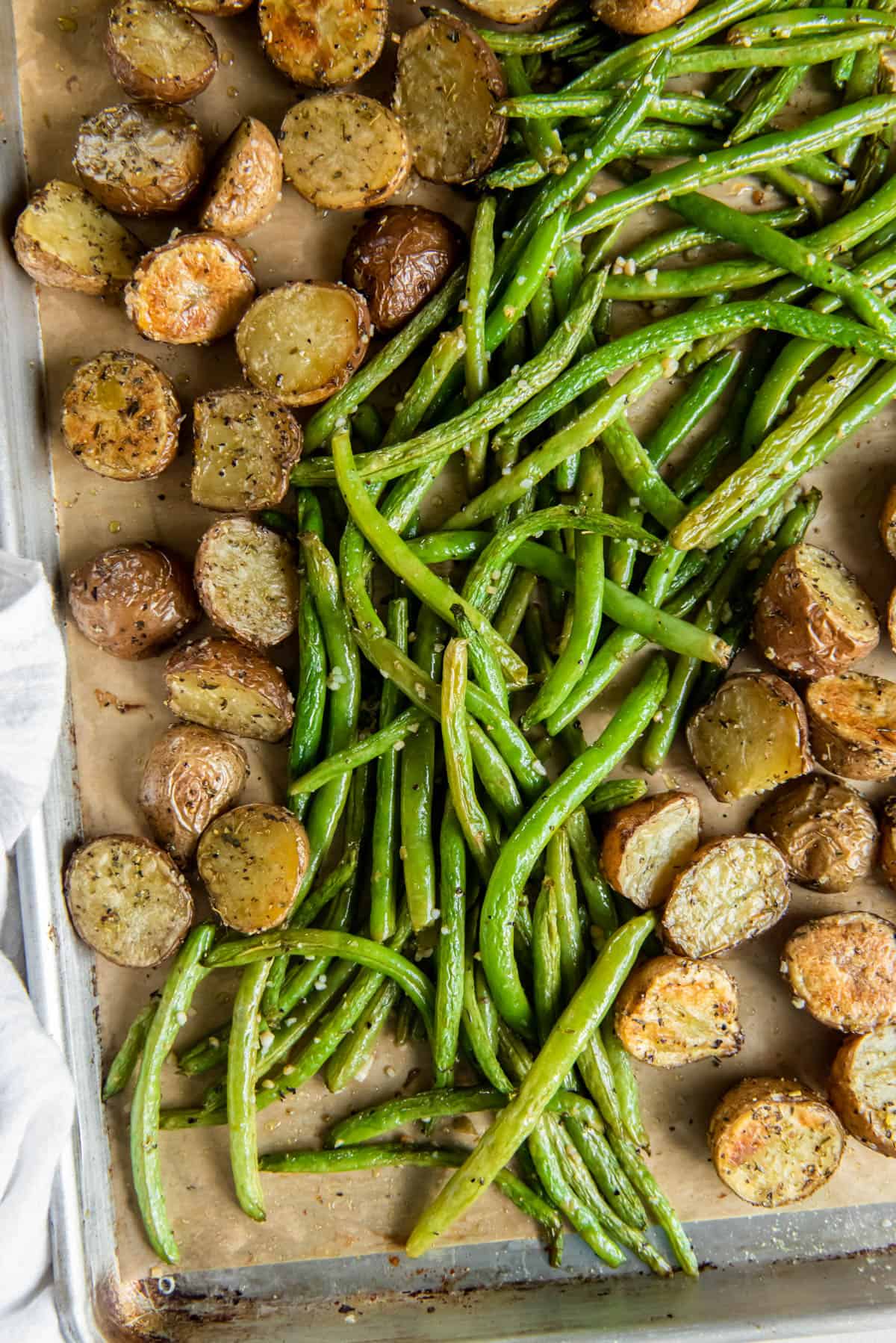 A sheet pan with roasted green beans and potatoes sitting on a white countertop after coming out of the oven.