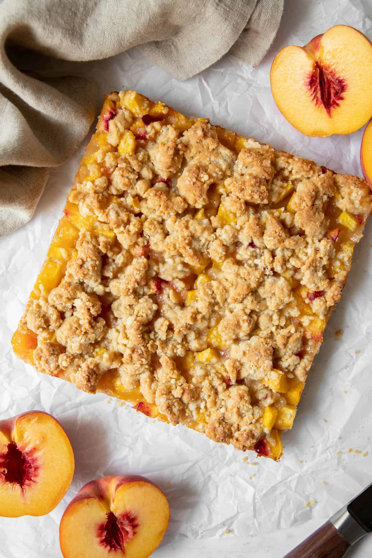 Peach bars after they have been baked sit on a piece of white parchment paper before cutting into squares with a knife.