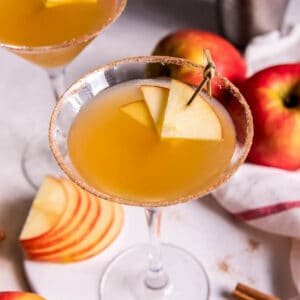 Two apple cider martinis on a countertop with a sliced apple on the side.