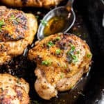 A spoon with melted butter sits in the cast iron skillet next to the cooked cast iron chicken thighs.