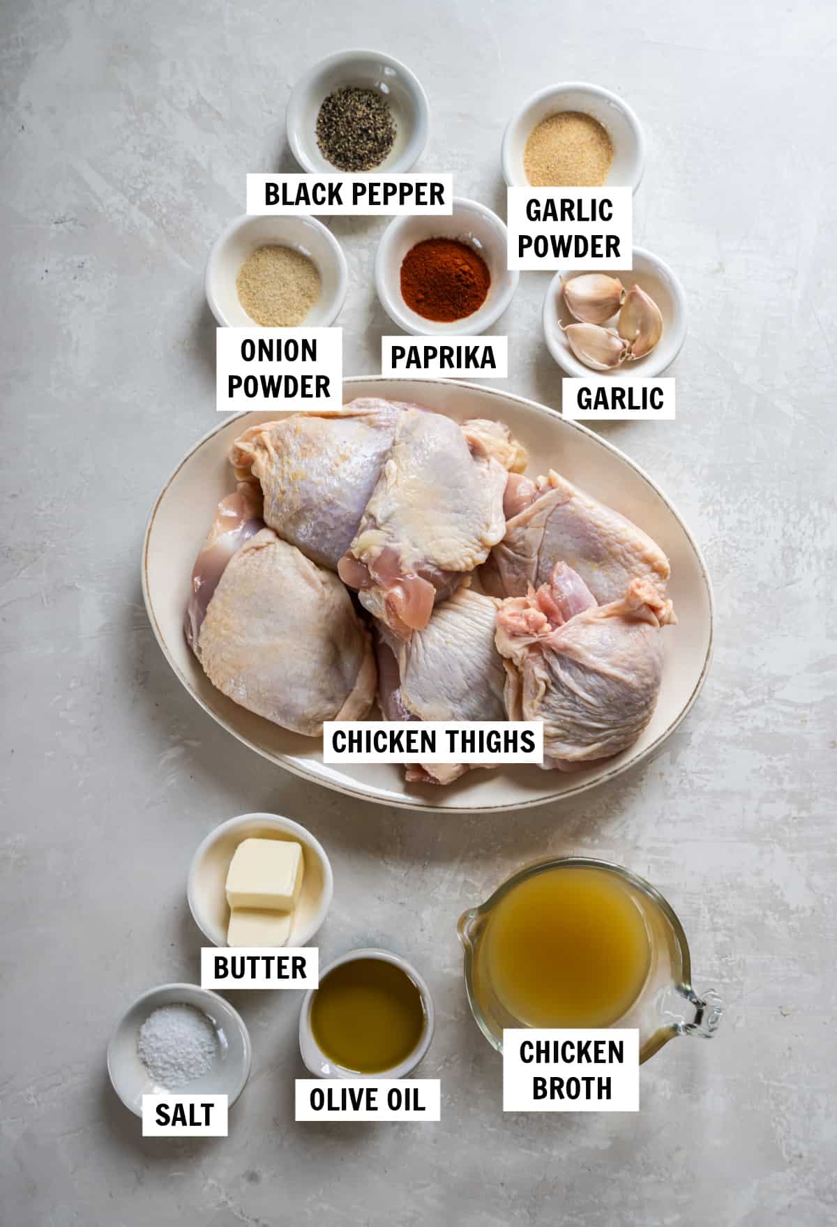 All of the ingredients you need for cast iron chicken thighs including chicken thighs, olive oil, butter, paprika, garlic powder, onion powder, salt, black pepper, garlic and chicken broth.