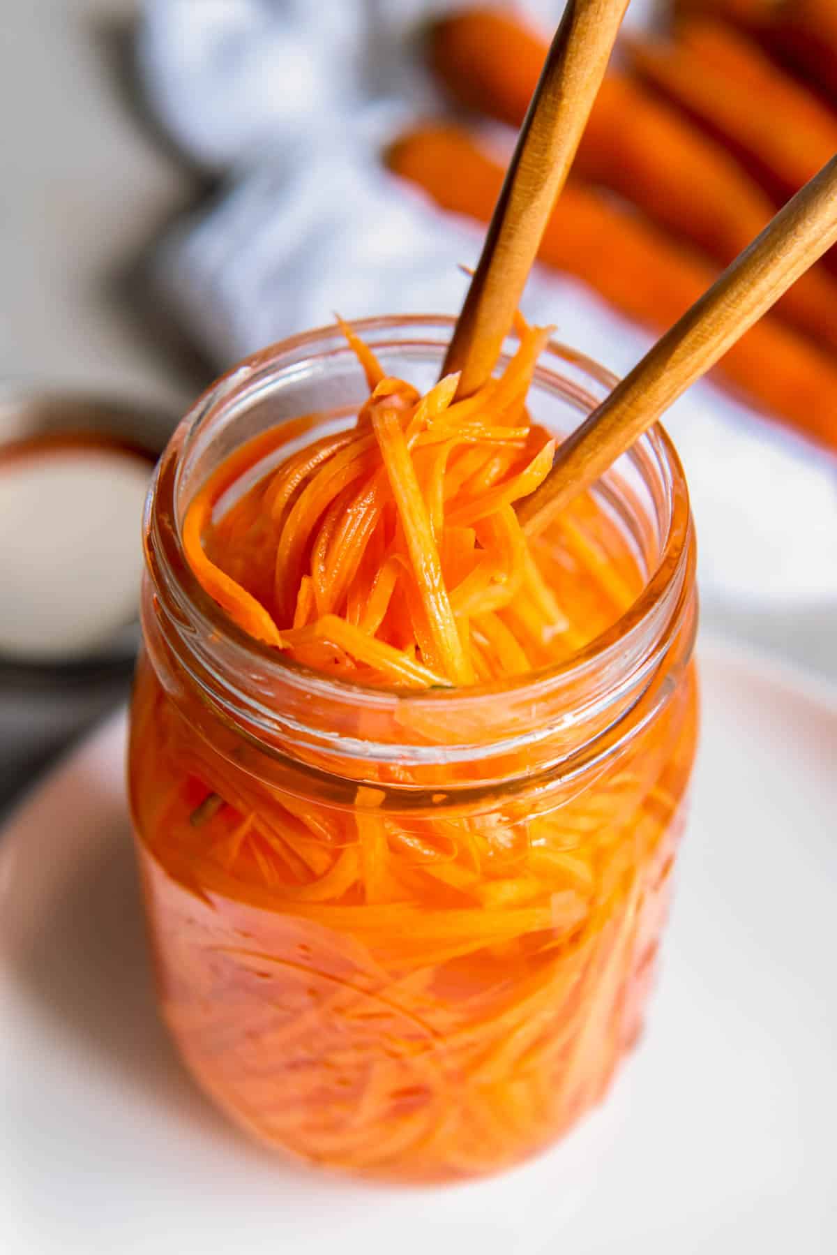 Two chopsticks picking up quick pickled carrots out of a mason jar for serving.