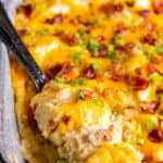 A casserole dish filled with twice baked mashed potatoes. A spoon is sitting in the dish ready to serve the mashed potatoes.