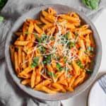 A bowl filled with tomato basil pasta with fresh Parmesan and basil sprinkled on top.
