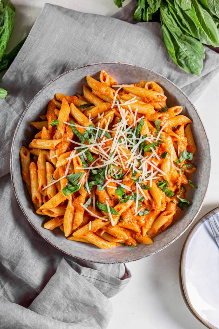 A bowl filled with tomato basil pasta with fresh Parmesan and basil sprinkled on top.