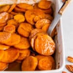Old Fashioned Candied Sweet Potatoes in a rectangular baking dish for serving. A spoon scoops out a few potatoes.