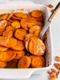 Old Fashioned Candied Sweet Potatoes in a rectangular baking dish for serving. A spoon scoops out a few potatoes.