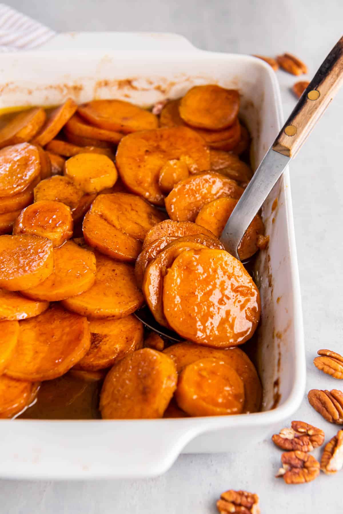 Old Fashioned Candied Sweet Potatoes in a rectangular baking dish for serving. A spoon scoops out a few potatoes.