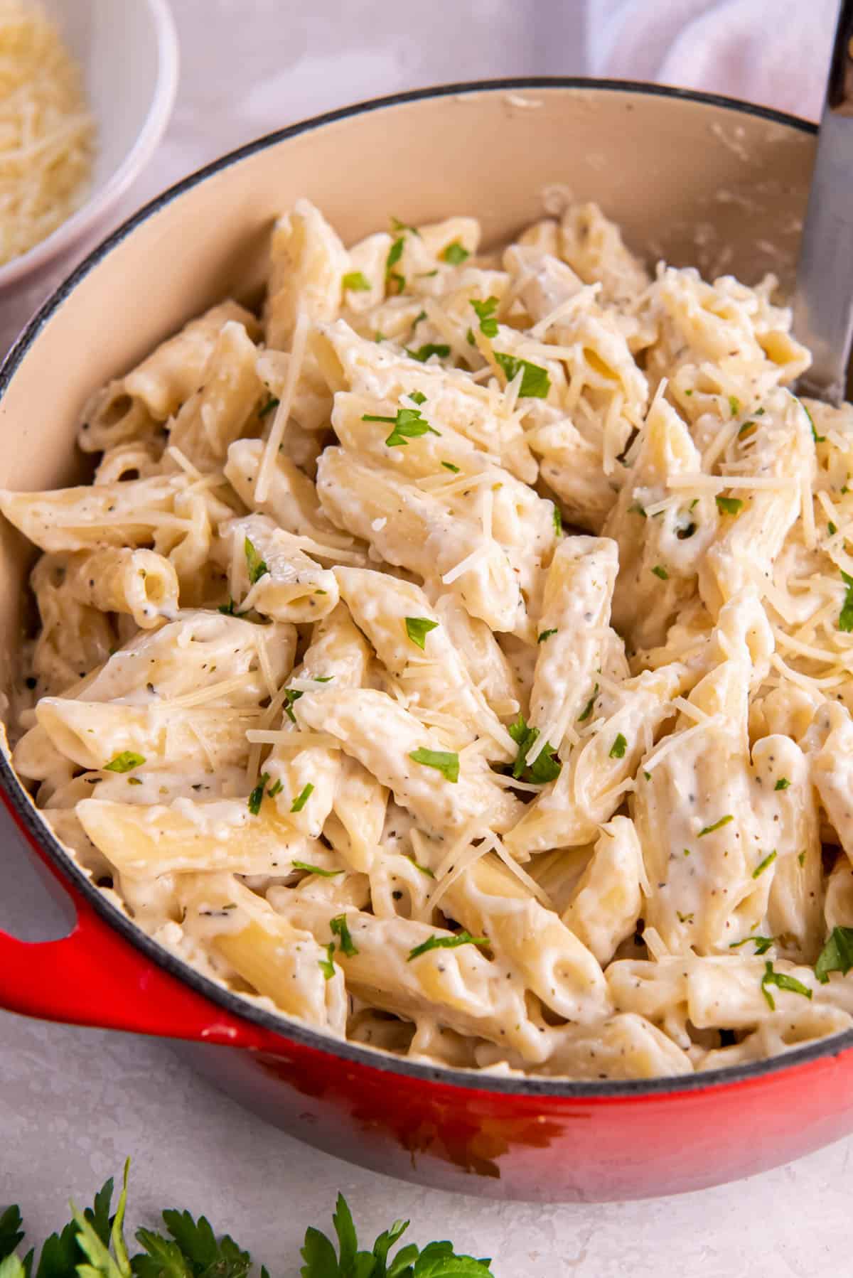 Alfredo penne pasta in a large pasta pan ready for serving. Freshly shredded Parmesan cheese is on top with freshly chopped parsley.