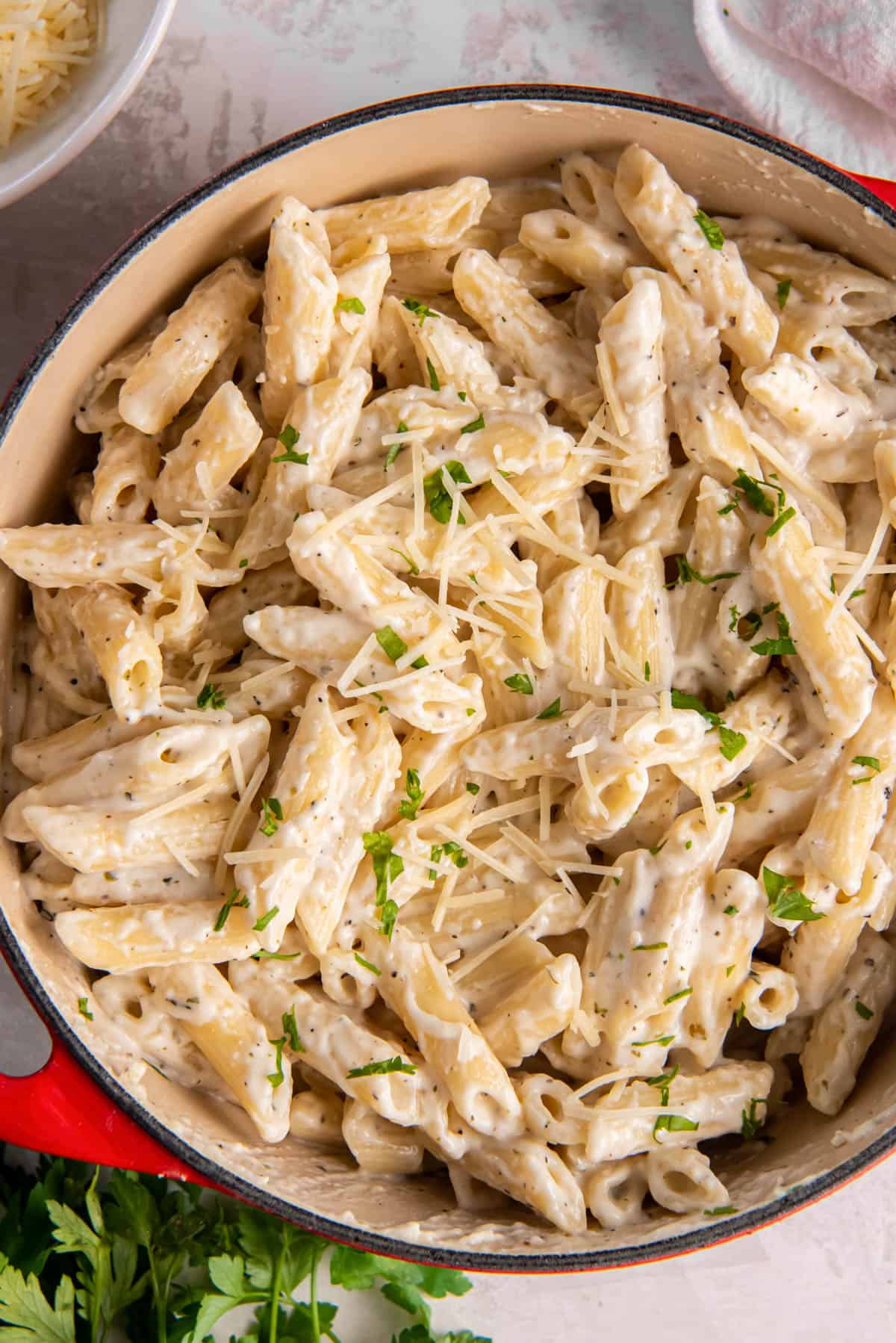 Alfredo penne pasta sits in a large pasta pan. It is sprinkled with Parmesan cheese for serving.