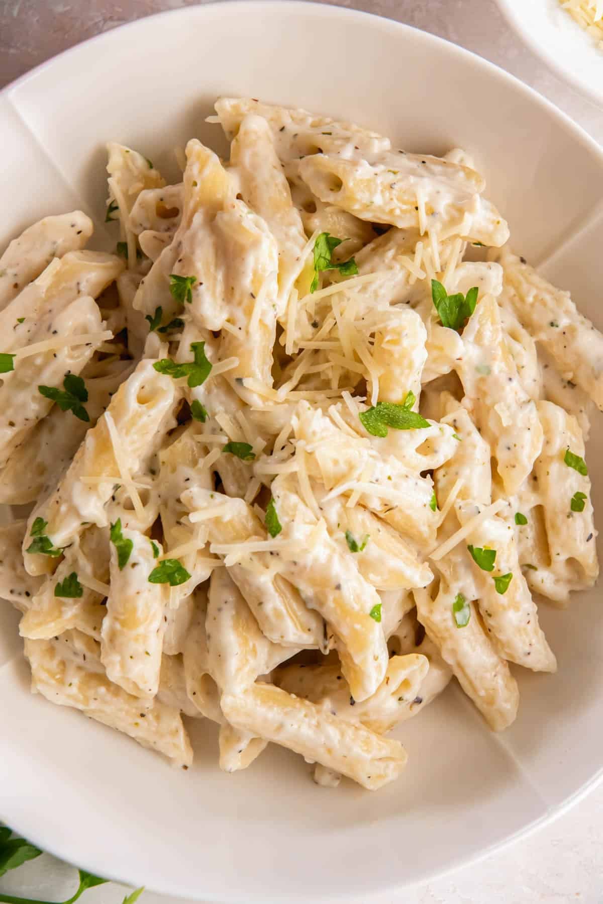 Creamy alfredo penne pasta served in a white bowl, topped with freshly grated Parmesan and chopped parsley.