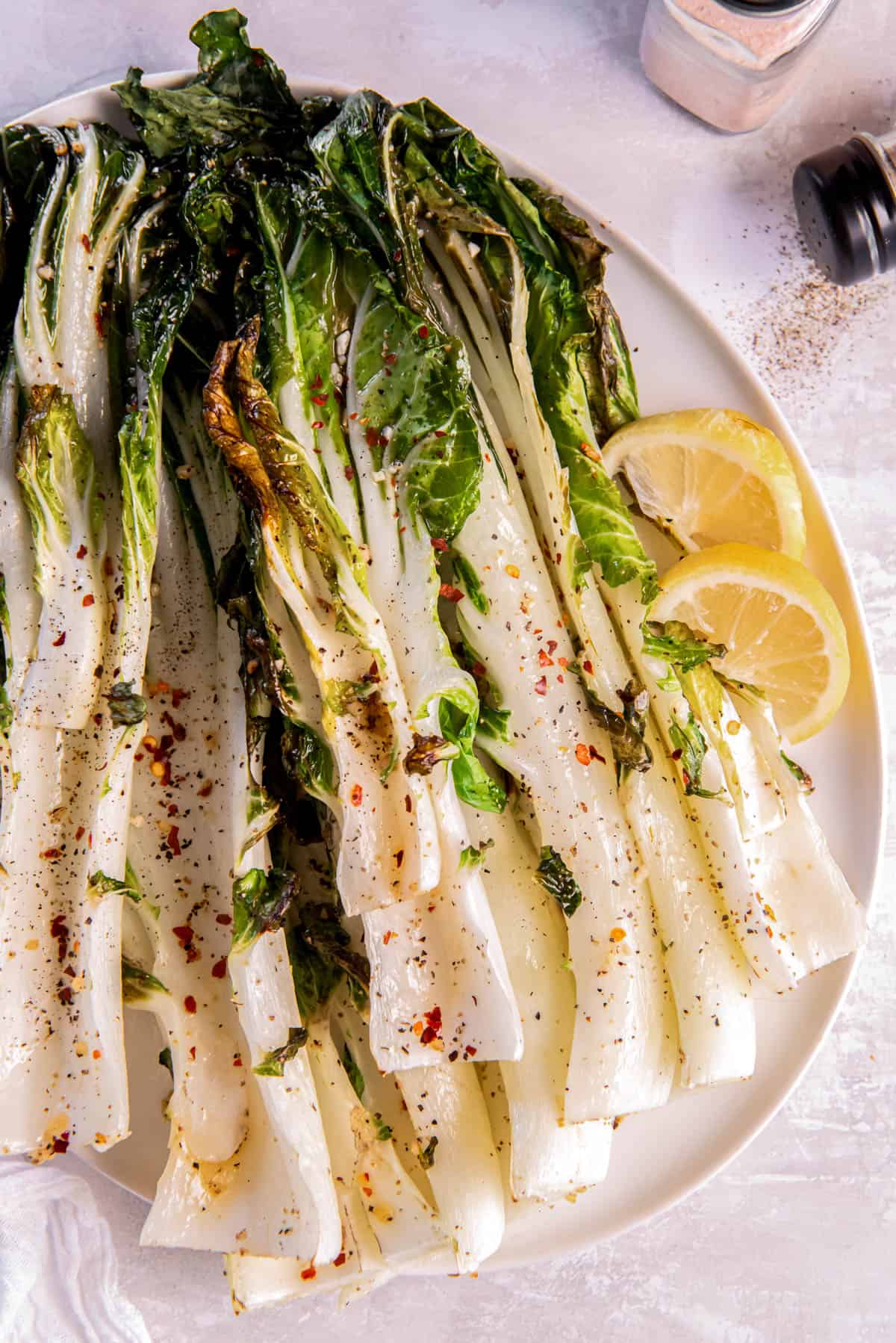 Roasted bok choy on a white plate with a slice of lemon for serving.
