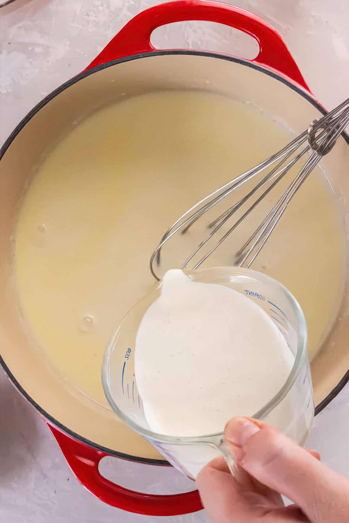 Milk and heavy cream being poured into a roux to create creamy Alfredo sauce.