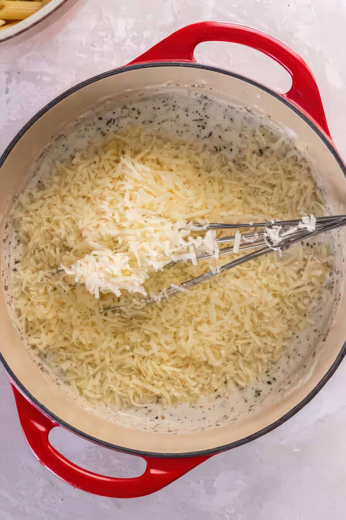 Freshly grated Parmesan cheese being stirred into warm Alfredo sauce until melted and smooth.