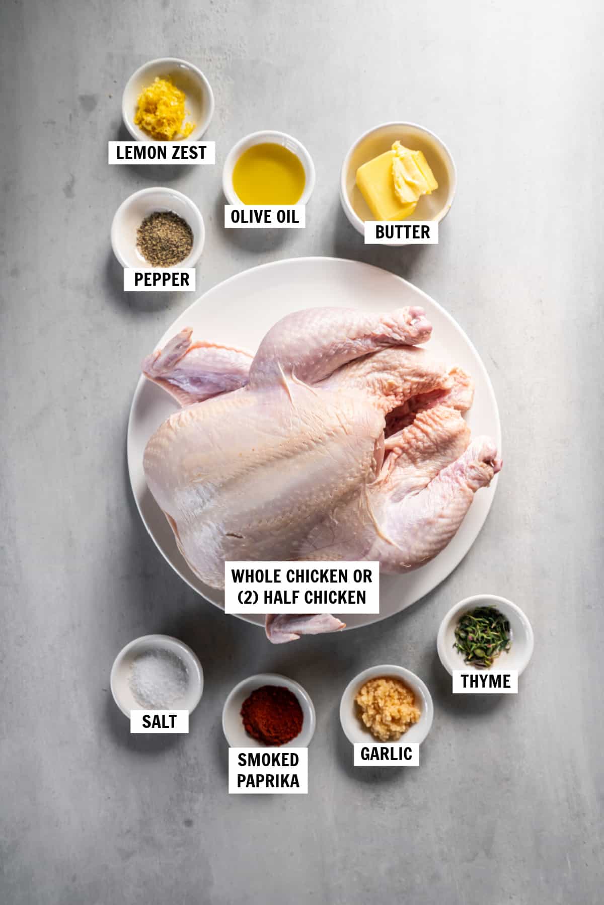 All of the ingredients for roasted half chicken sitting in bowls on a countertop including whole chicken, lemon zest, olive oil, butter, salt and pepper, smoked paprika, garlic and thyme.