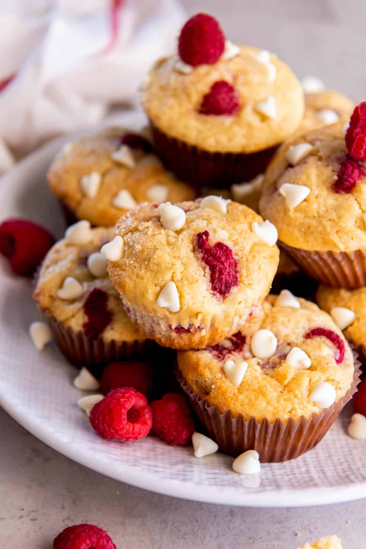 Raspberry and white chocolate muffins sitting on a serving plate with fresh raspberries garnished on top.