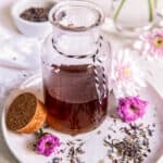 Vanilla lavender simple syrup in a glass jar sitting on a small plate with fresh lavender buds sitting to the side.