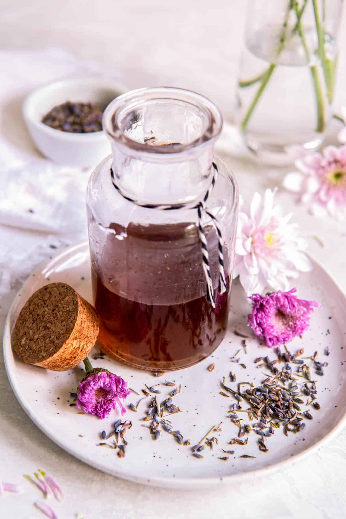 Vanilla lavender simple syrup in a glass jar sitting on a small plate with fresh lavender buds sitting to the side.