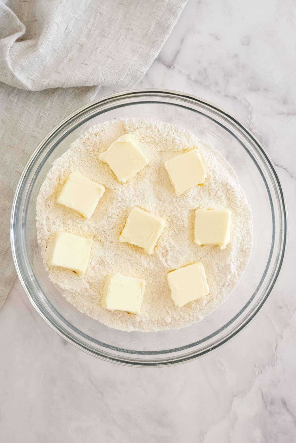 Butter cubes scattered over flour in a glass bowl before cutting in to make coffee cake muffin streusel.