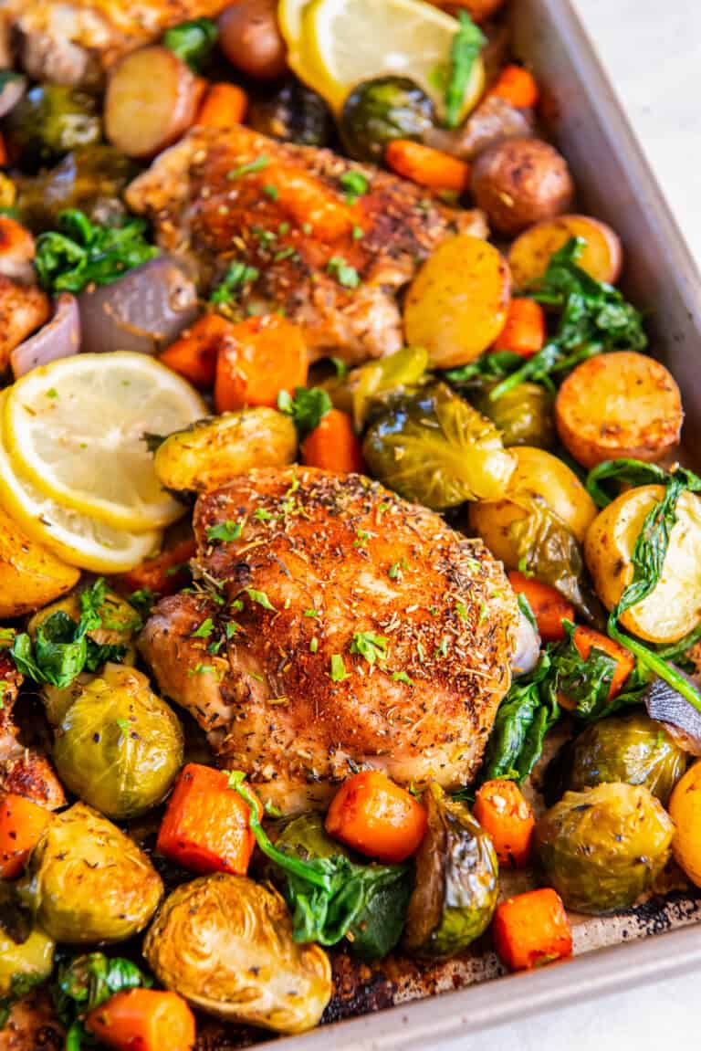Sheet pan chicken thighs with vegetables like carrots, brussels sprouts, red onion and potatoes on a sheet pan after baking.