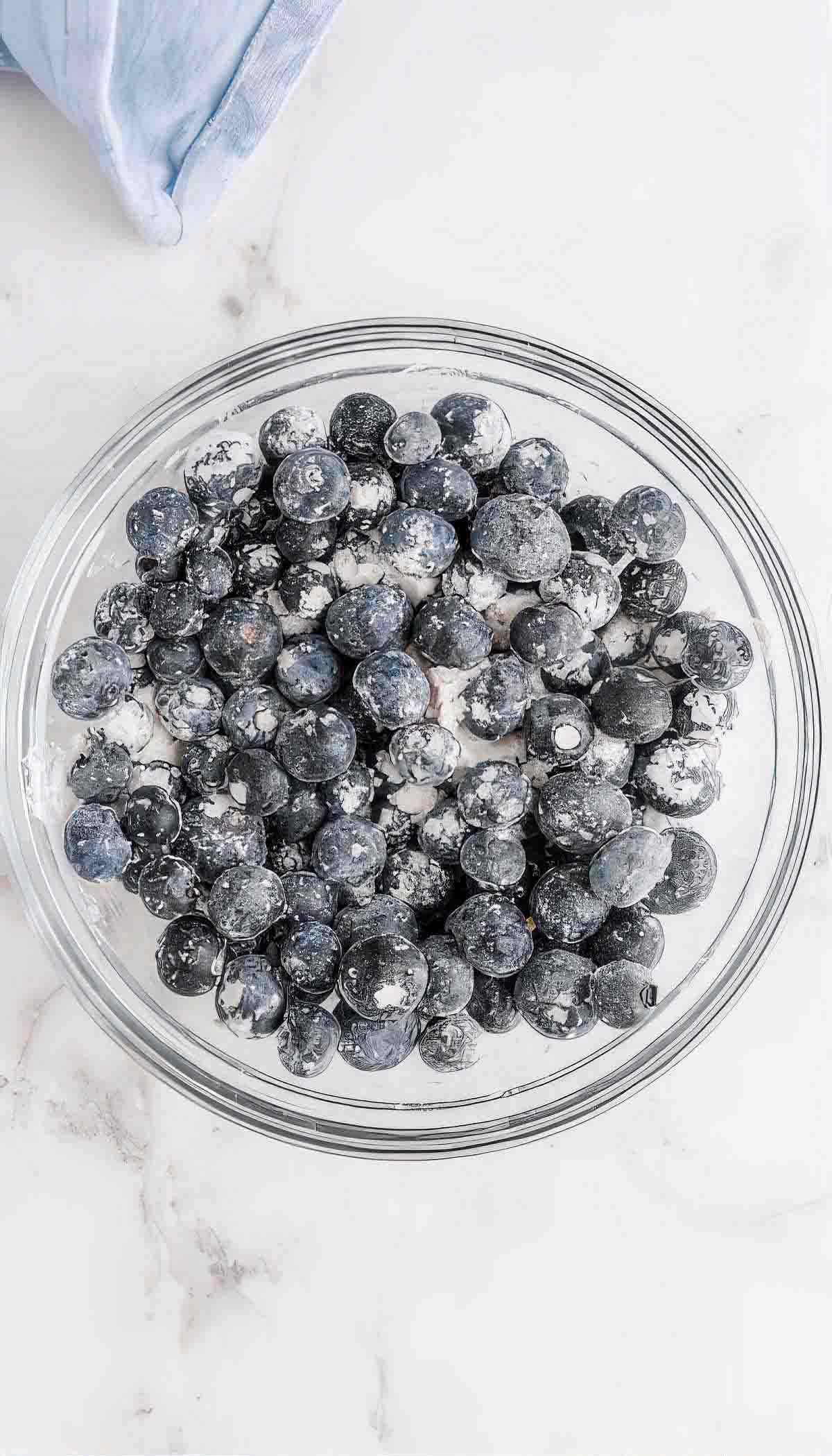 Fresh blueberries tossed with flour in a glass bowl for buttermilk blueberry breakfast cake.