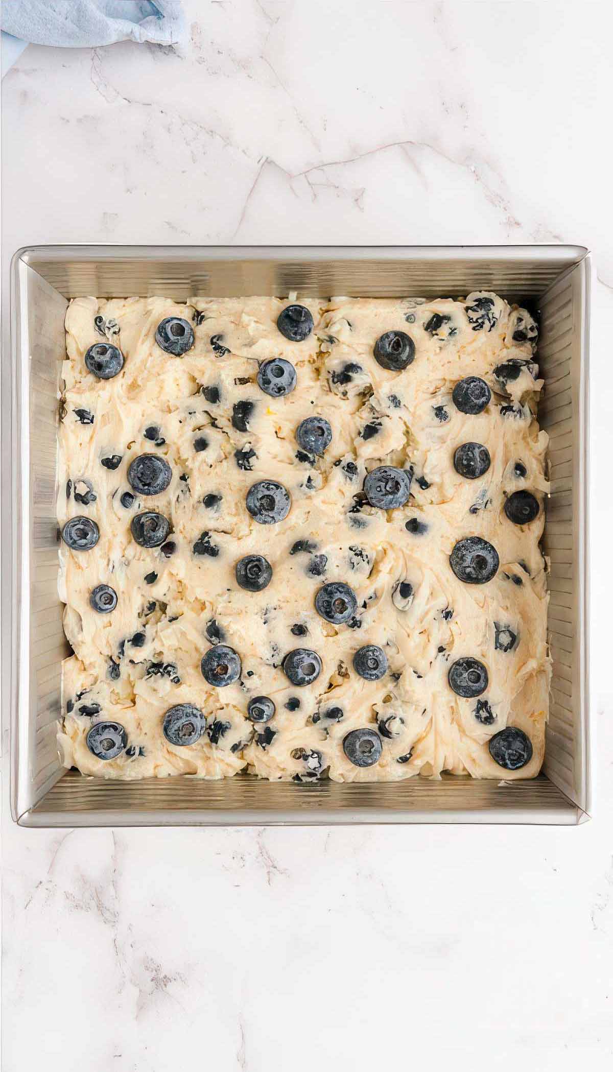Blueberry breakfast cake batter spread into a square baking pan before baking.