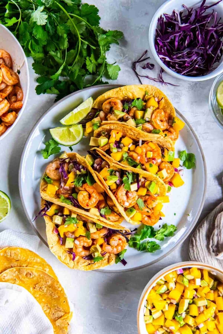 Cilantro lime shrimp tacos with mango avocado salsa served on a plate with lime wedges and fresh cilantro