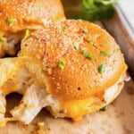 A Hawaiian roll sandwich with chicken and melted cheese in it. It is sprinkled with parmesan cheese. It is on a tray with parchment paper.