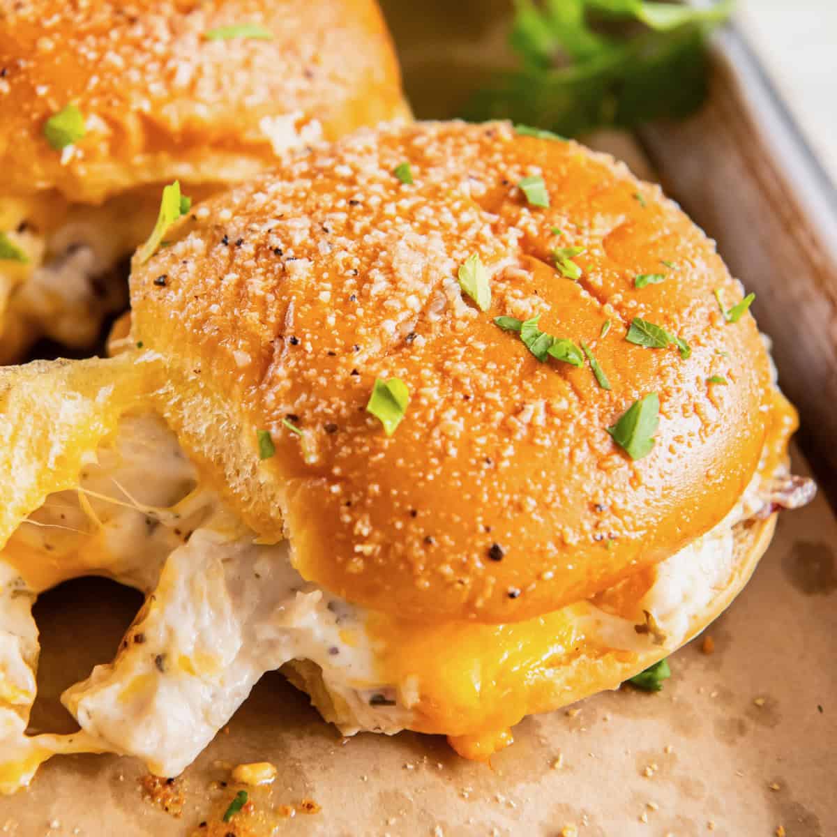 A Hawaiian roll sandwich with chicken and melted cheese in it. It is sprinkled with parmesan cheese. It is on a tray with parchment paper.