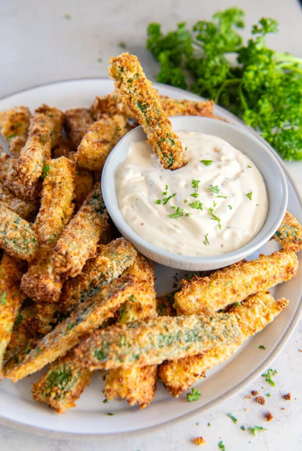 A plate of battered and fried zucchini fries on a white plate with aioli.