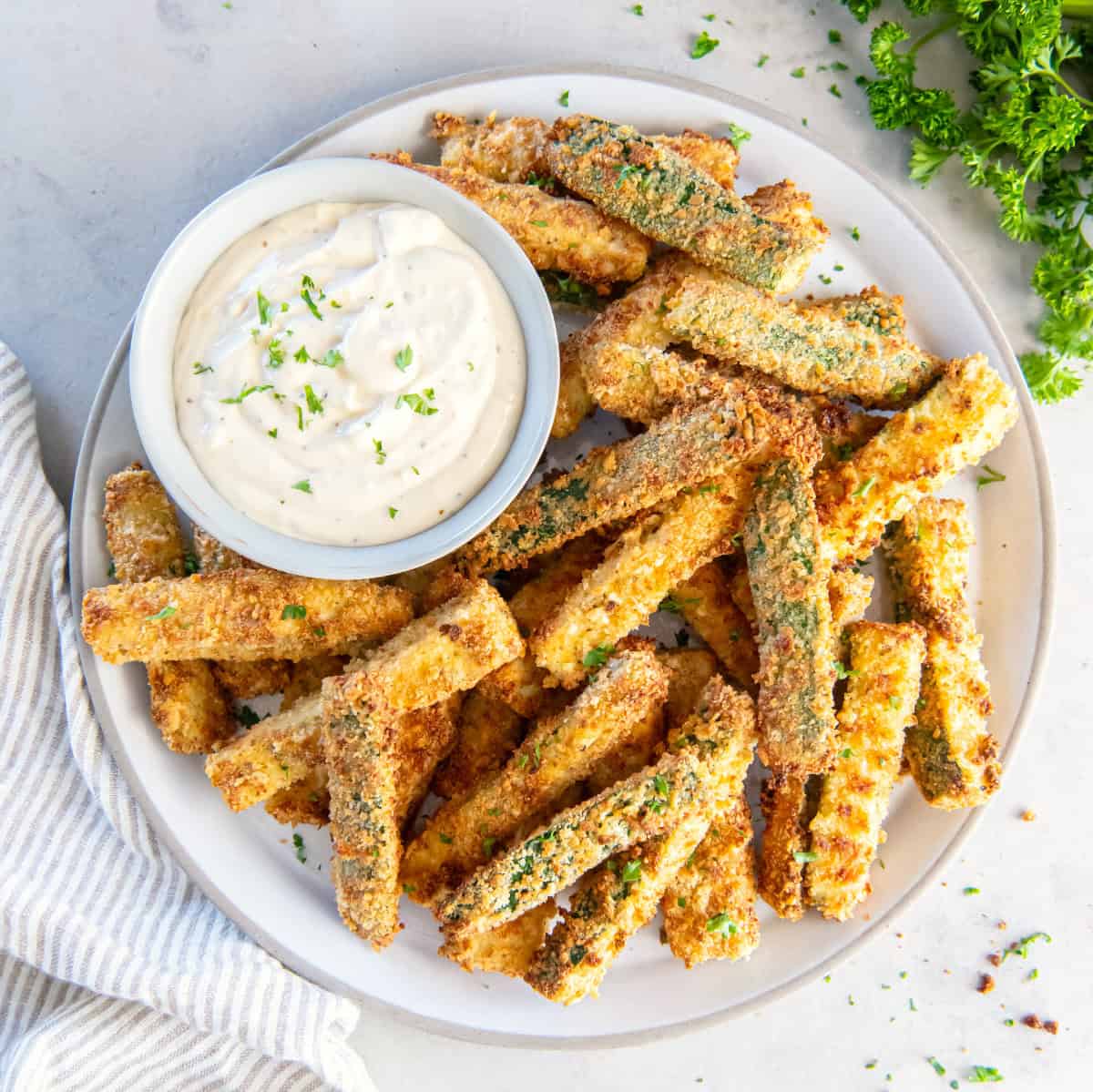 A plate of battered and fried zucchini fries on a white plate with aioli.