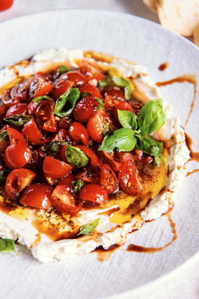 Close-up of bruschetta dip on toasted bread with creamy cheese, tomatoes, and basil.
