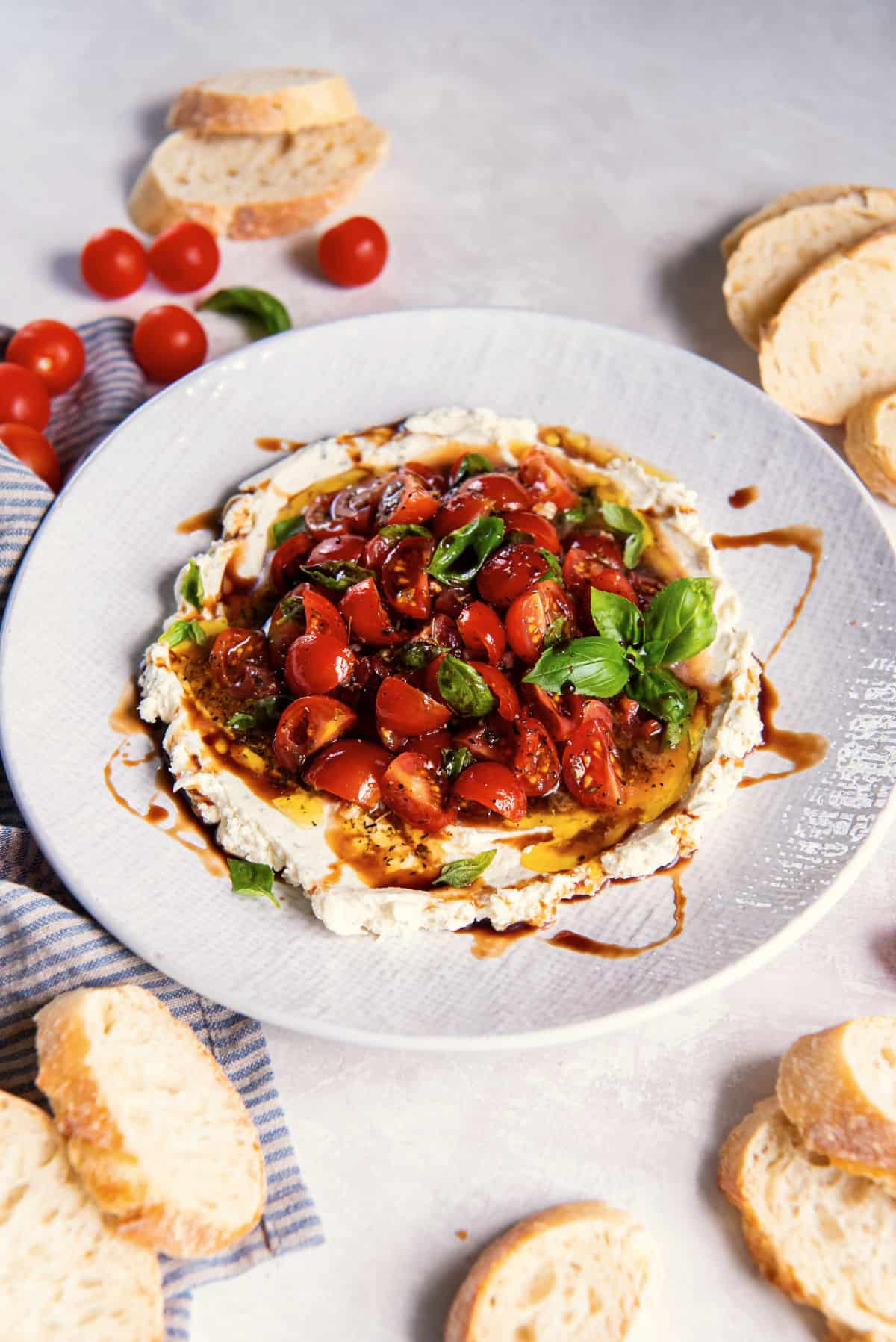 Angled view of bruschetta dip showing layers of creamy cheese, tomato topping, and fresh herbs.